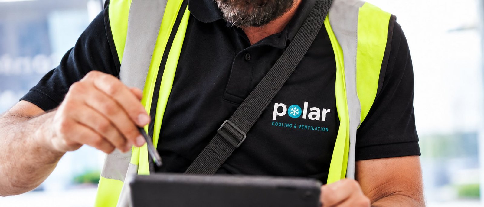 Polar engineer in branded polo and hi-vis completing a job report on a tablet