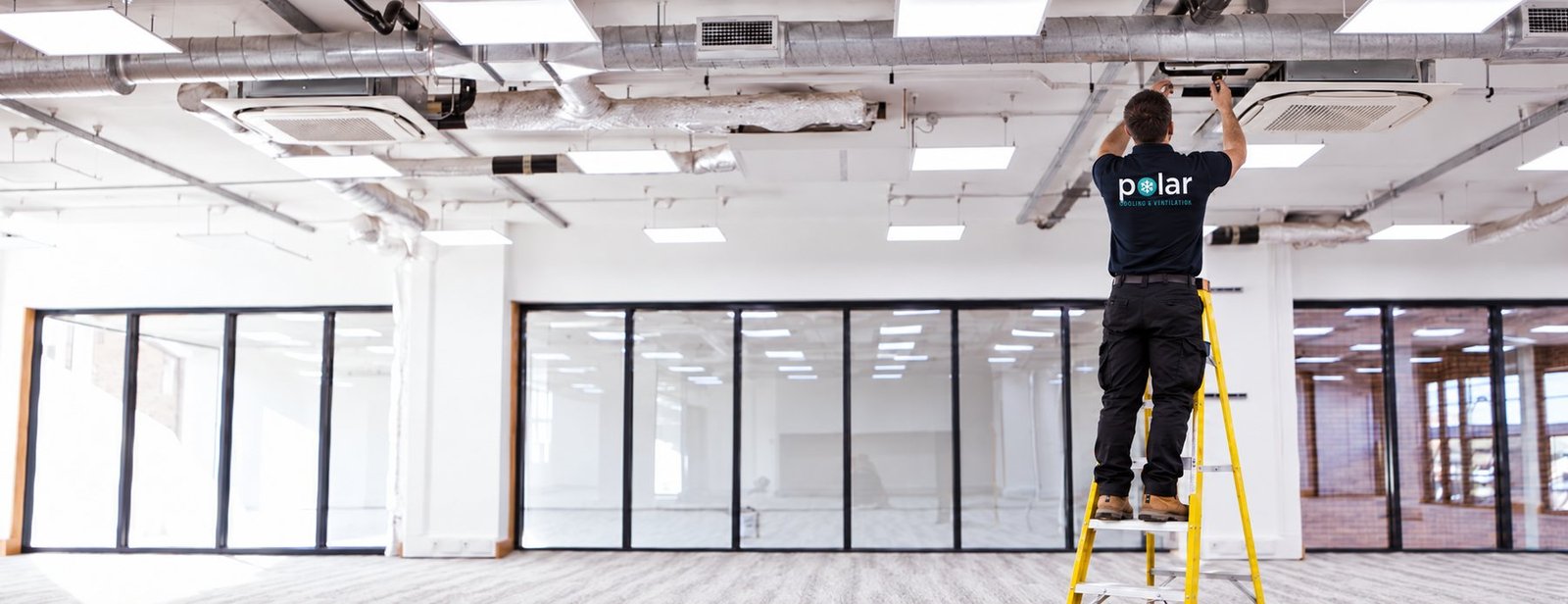 Polar engineer on a ladder installing a cassette unit in an open-plan office